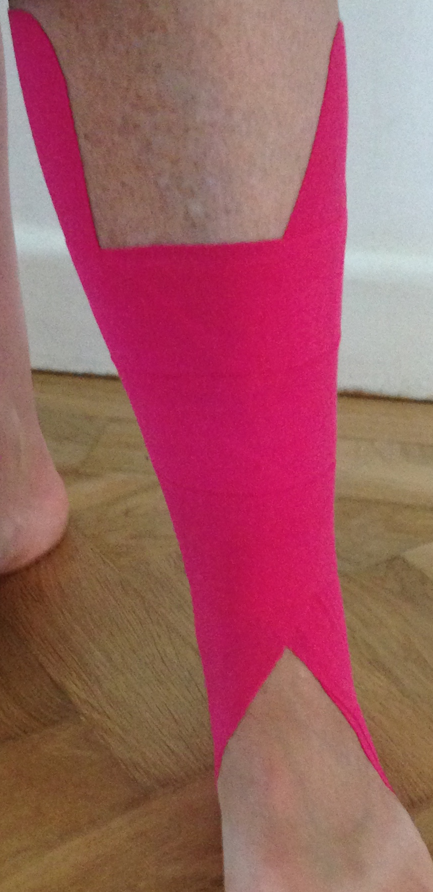 A single tall pink kinesio tape strip up the back of an Achilles and calf